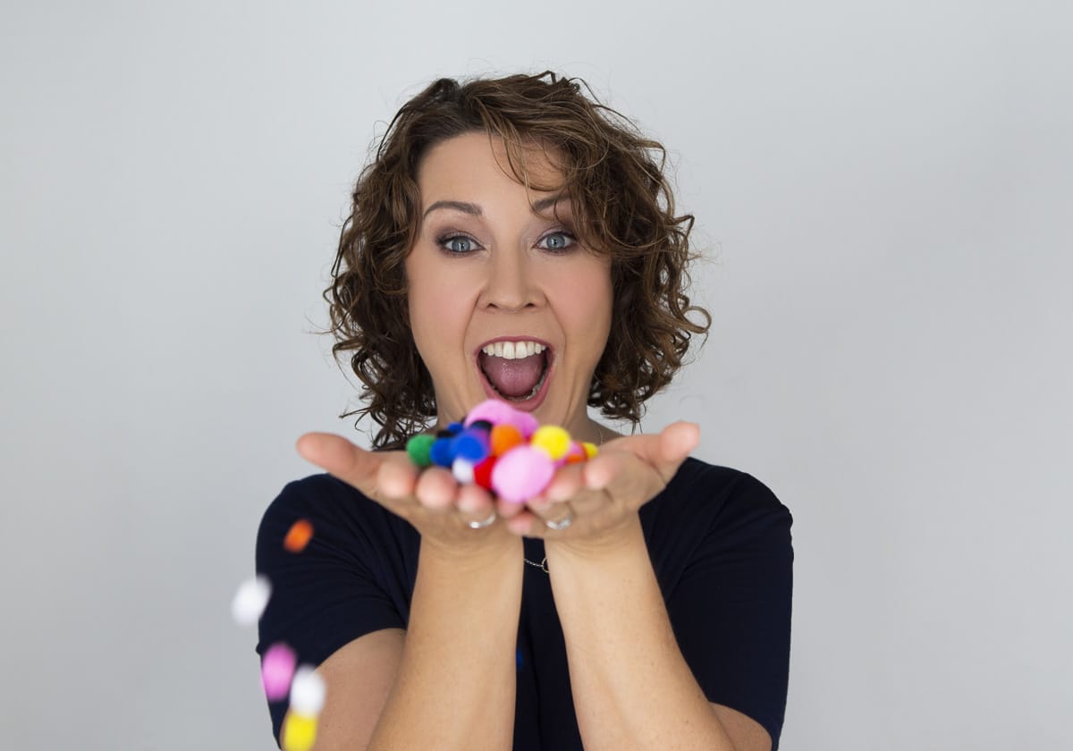 Stef holding multi-coloured pom poms.