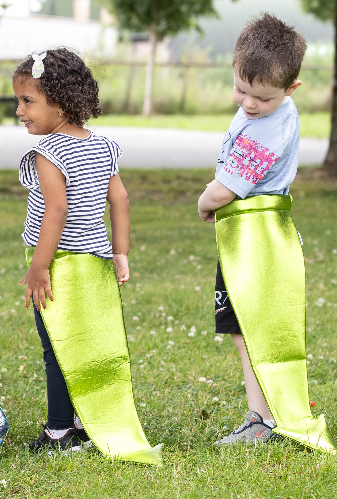 Tow children wearing colourful costume tails in a park setting