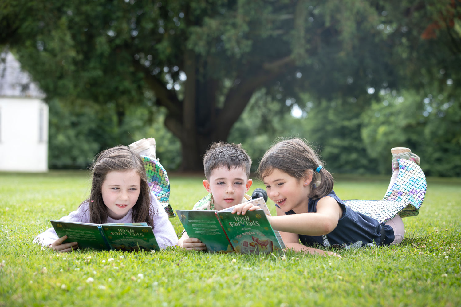 Three children lying on grass reading Irish Fairy Tails books