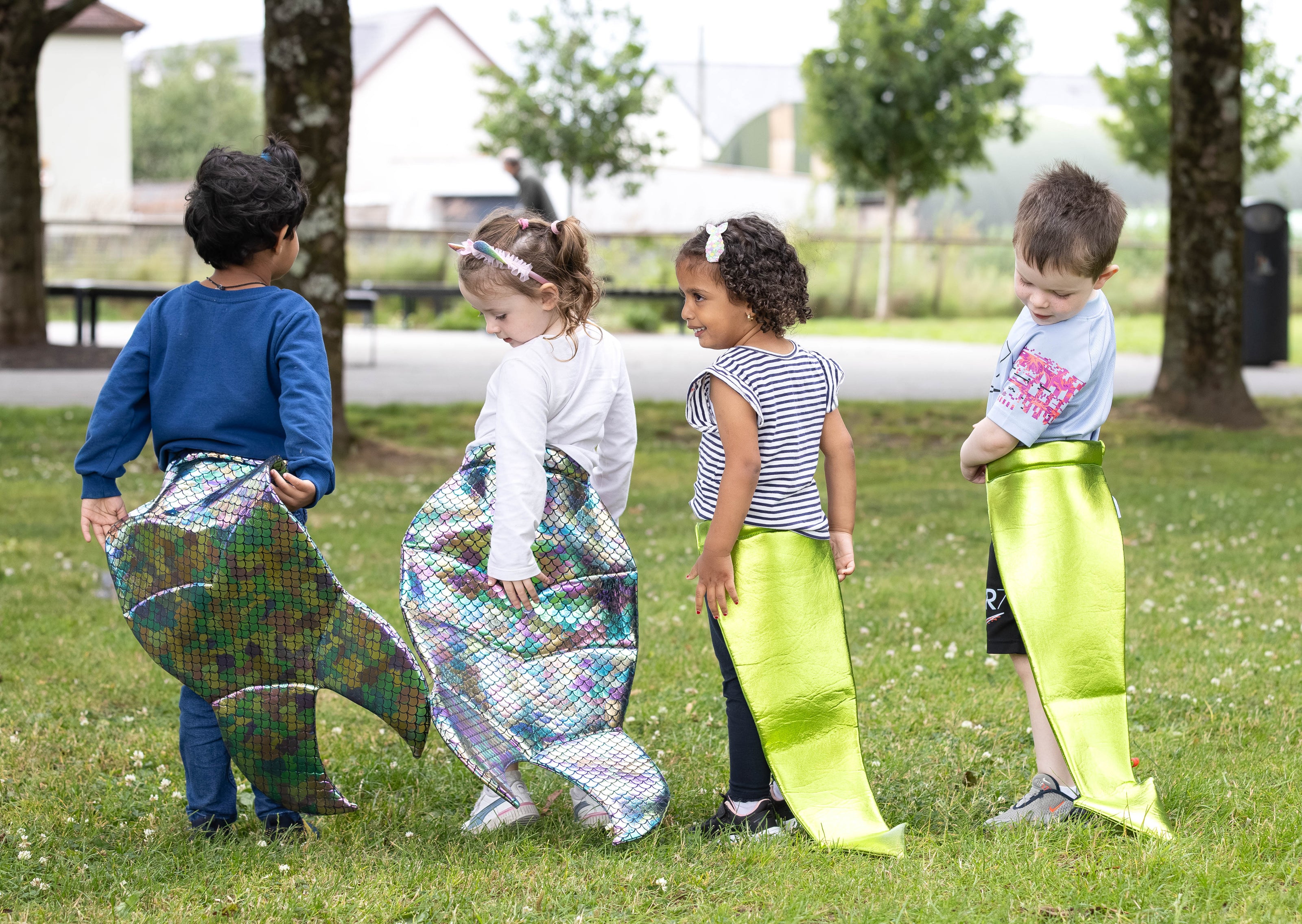Four children wearing dress up mermaid tails and dragon tails in a park setting