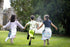 Three children running together wearing dragon tails and mermaid tails in a park with a castle in the background