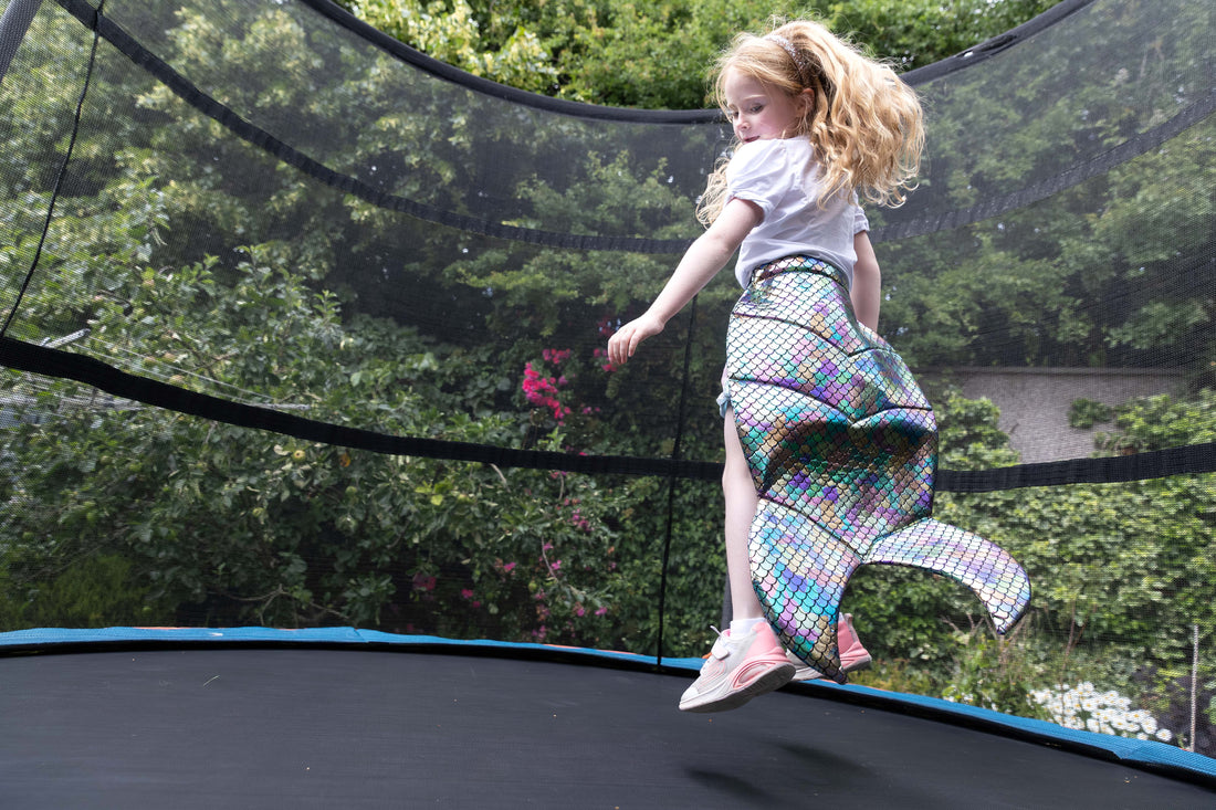 Child jumping on a trampoline with a colorful mermaid tail