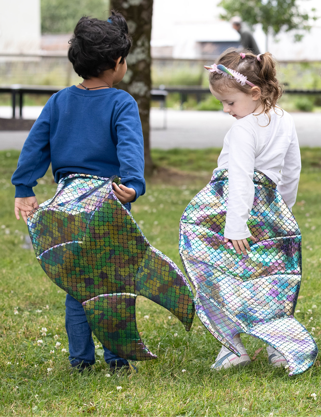Two children playing outdoors with colorful mermaid tails.
